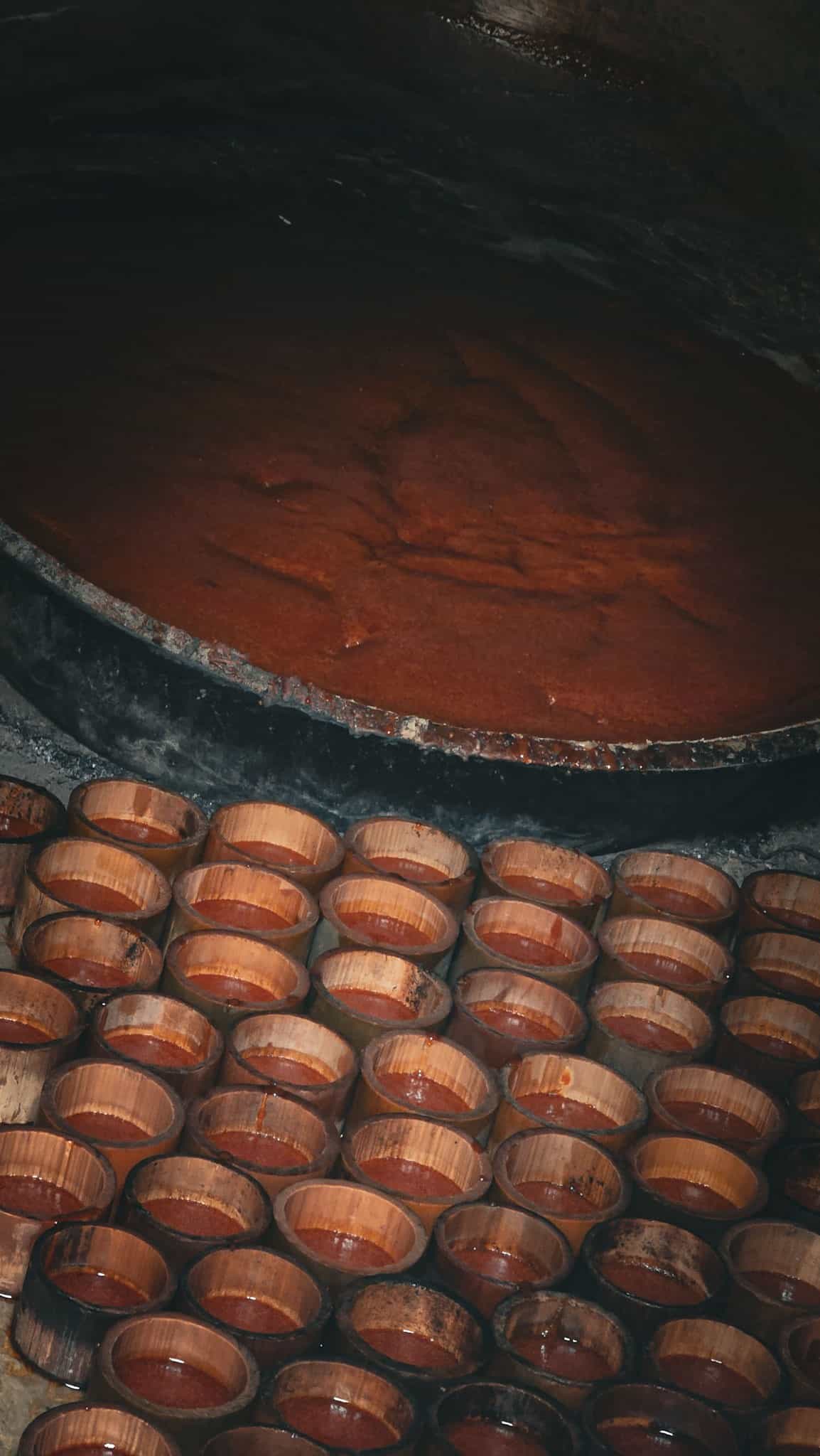 Palm sap reducing in a wide iron wok with bamboo moulds in the foreground