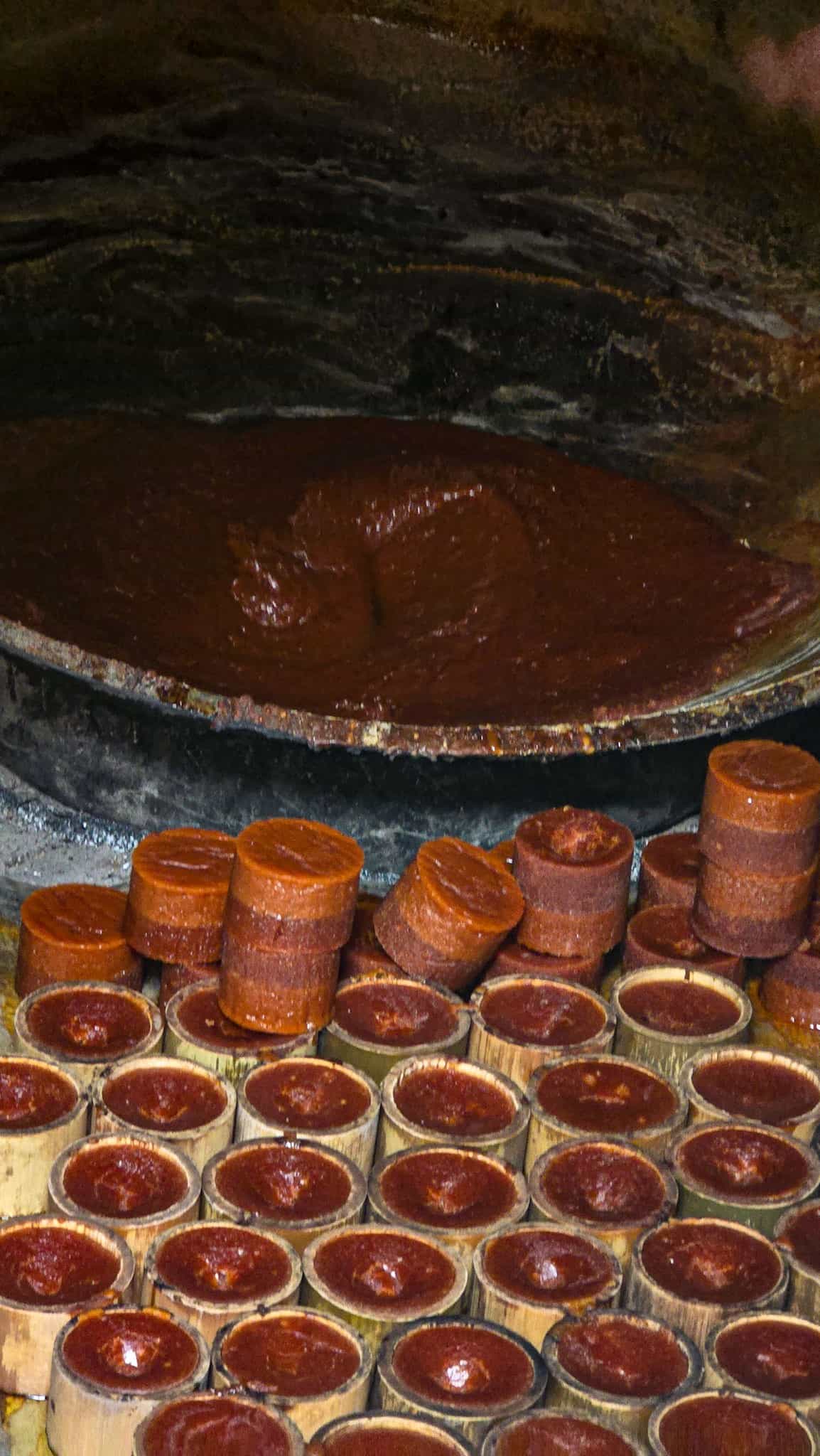 Palm sugar sap reducing in a wide iron wok beside rows of sugar hardening in bamboo moulds